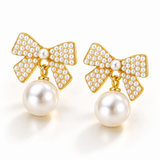 Pair of pearl bow drop earrings with gold-tone detailing on an elegant ivory background.