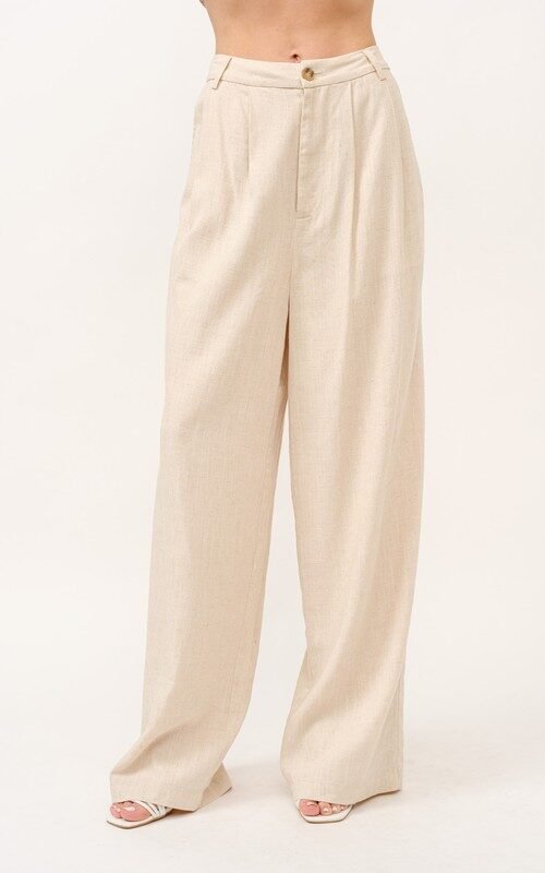 A woman stands facing forward, modeling the And The Why high-rise wide leg linen blend pants in beige, paired with a simple black top.