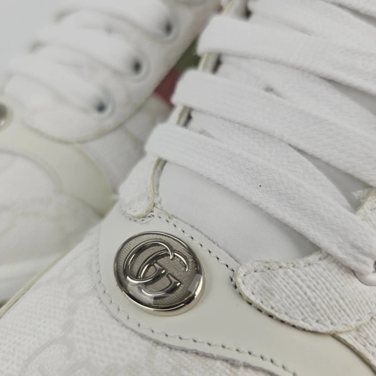 A close-up of the women's Gucci Screener sneakers, showcasing the GG logo, vintage finish, and the gold-toned logo detail.